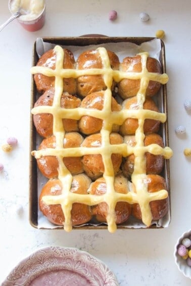 12 mini egg chocolate hot cross buns in a lined oven tray with more mini eggs on the side.