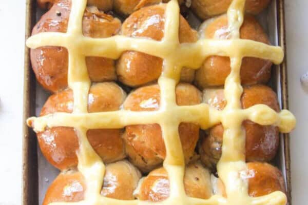 12 mini egg chocolate hot cross buns in a lined oven tray with more mini eggs on the side.