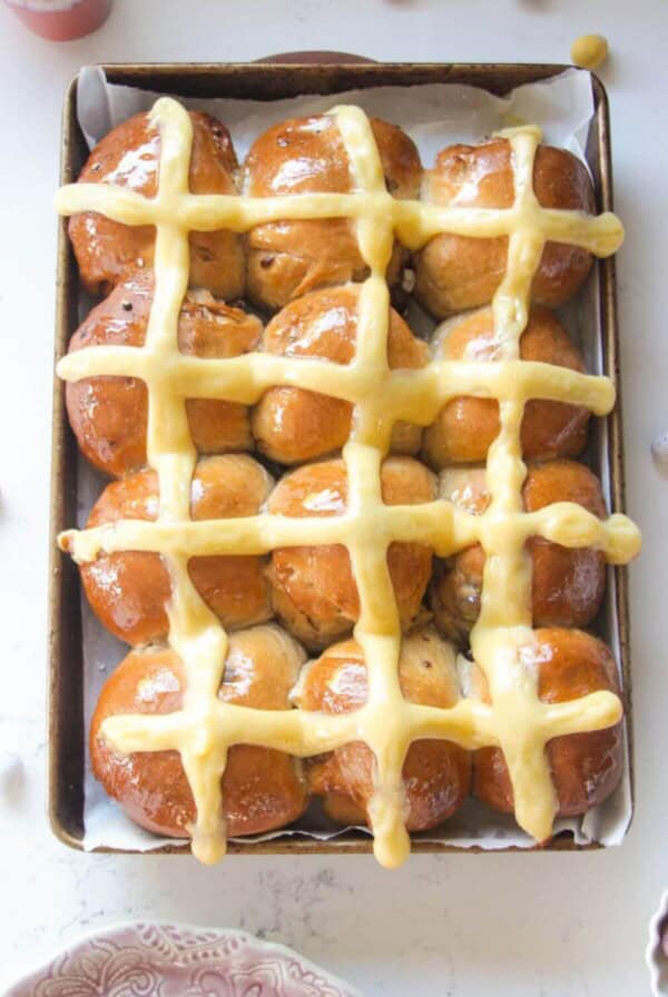 12 mini egg chocolate hot cross buns in a lined oven tray with more mini eggs on the side.