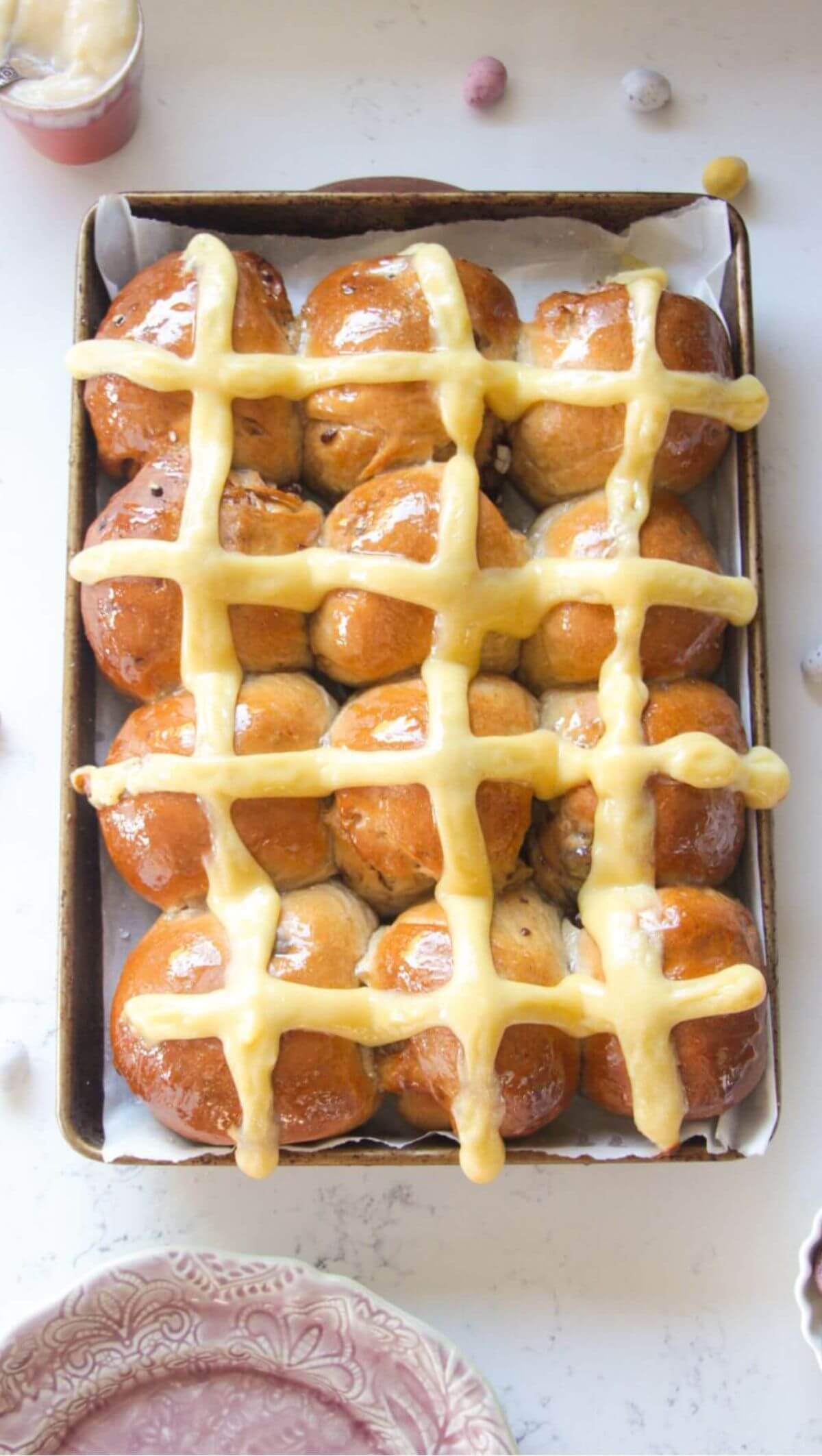 12 mini egg chocolate hot cross buns in a lined oven tray with more mini eggs on the side.