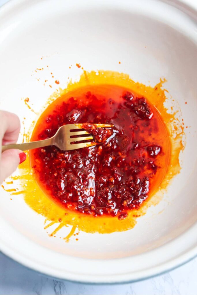 Harissa honey marinde ingredients being mixed with a fork in a large white bowl.