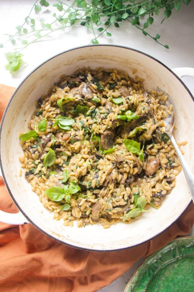Mushroom orzo in a large white skillet with a large silver spoon.