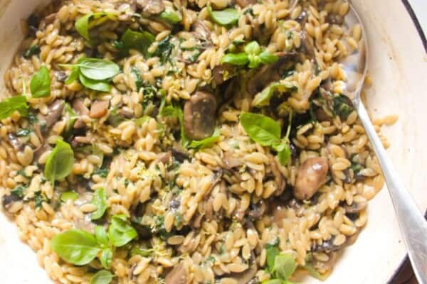 Mushroom orzo in a large white skillet with a large silver spoon.