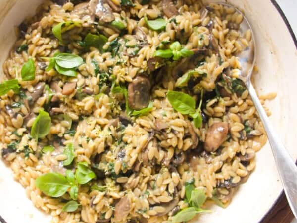 Mushroom orzo in a large white skillet with a large silver spoon.