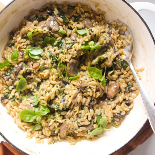 Mushroom orzo in a large white skillet with a large silver spoon.