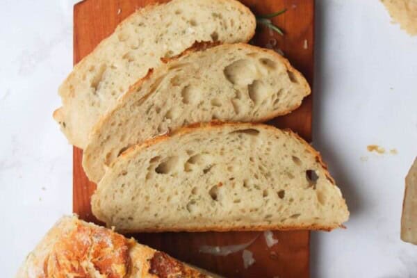 3 slices of bread on a small wooden board with the rest of the loaf and garlic butter in the background.