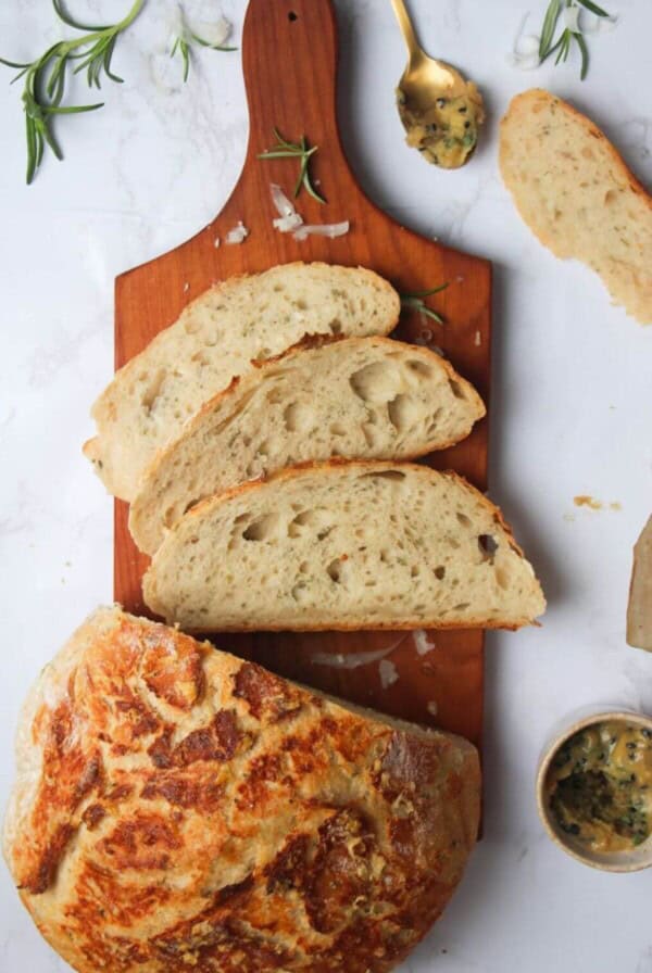 3 slices of bread on a small wooden board with the rest of the loaf and garlic butter in the background.
