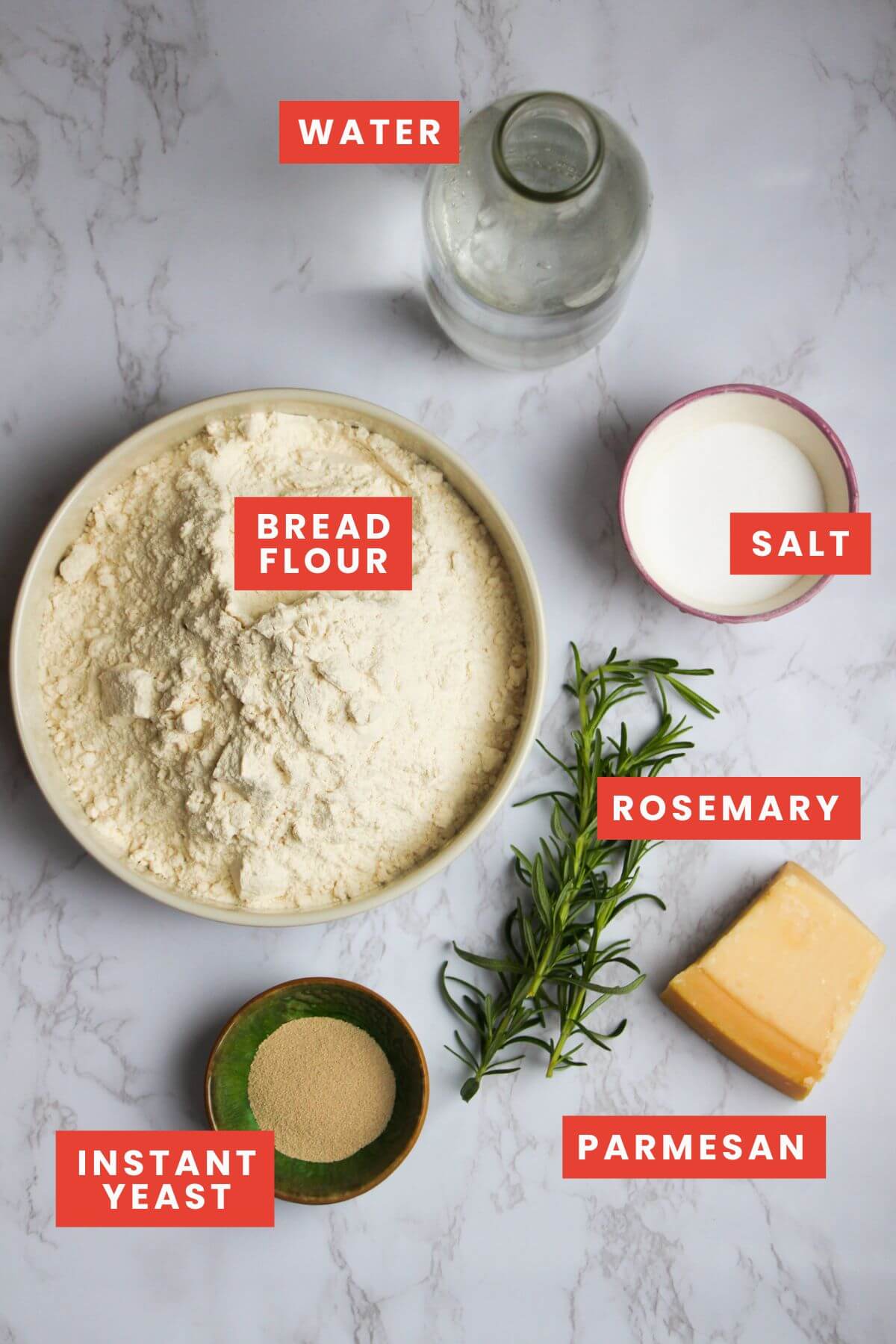 Ingredients for rosemary parmesan bread on a white marble background and labelled.