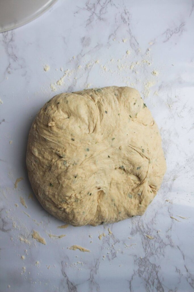 Shaped rosemary parmesan bread dough on a white marble background.