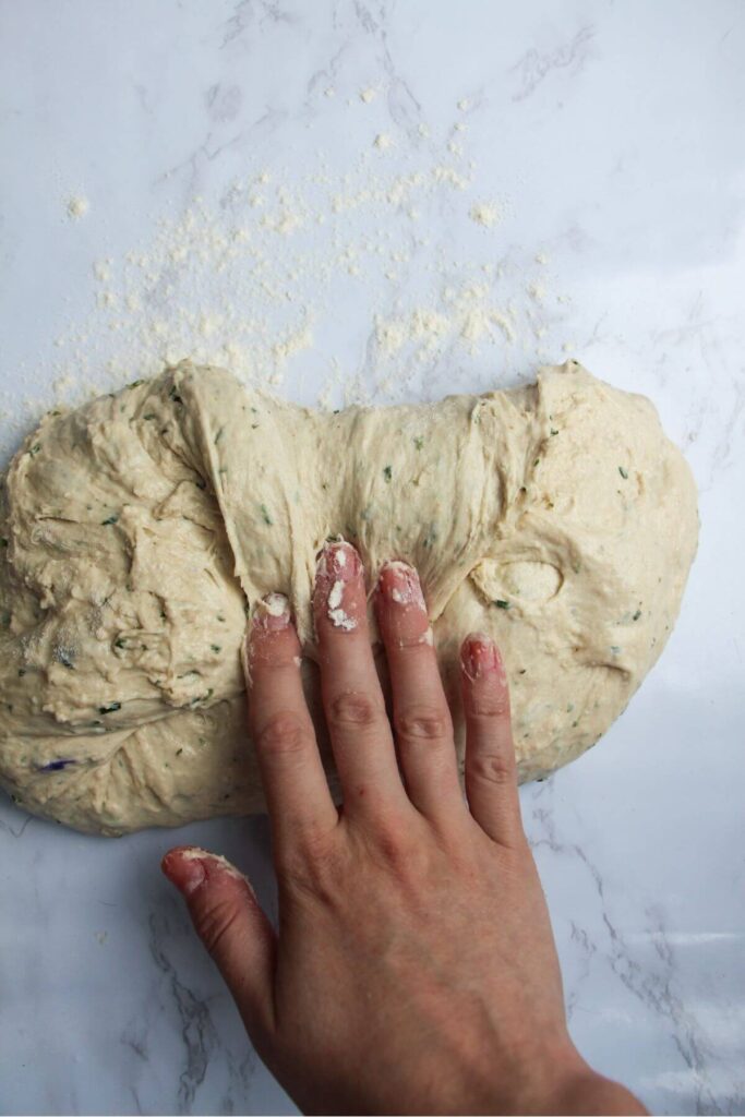 Hand shaping bread dough on a white marble background.