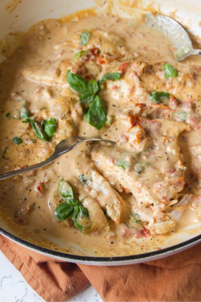 Close up of sliced chicken breast in creamy sundried tomato sauce in a large white skillet.