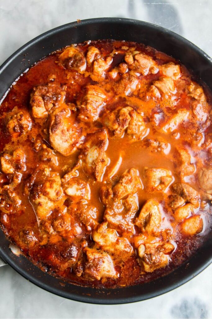 Stock and passata added to diced chicken and spices in a small frying pan.