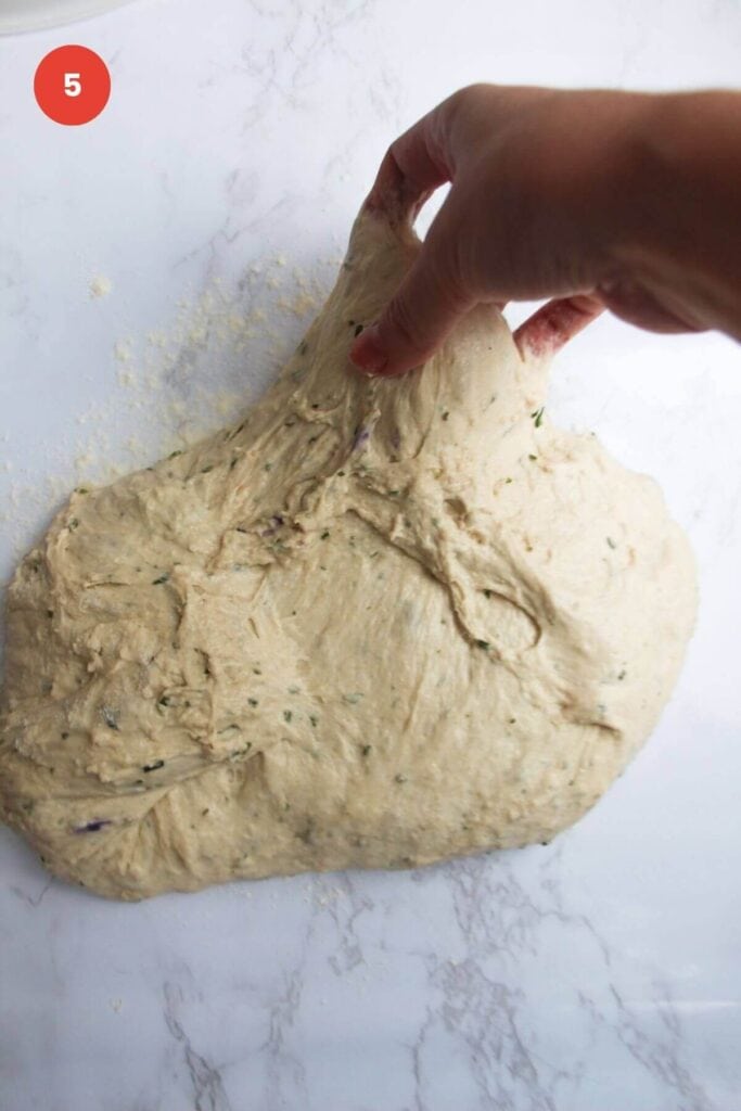 Hand stretching rosemary parmesan bread dough.