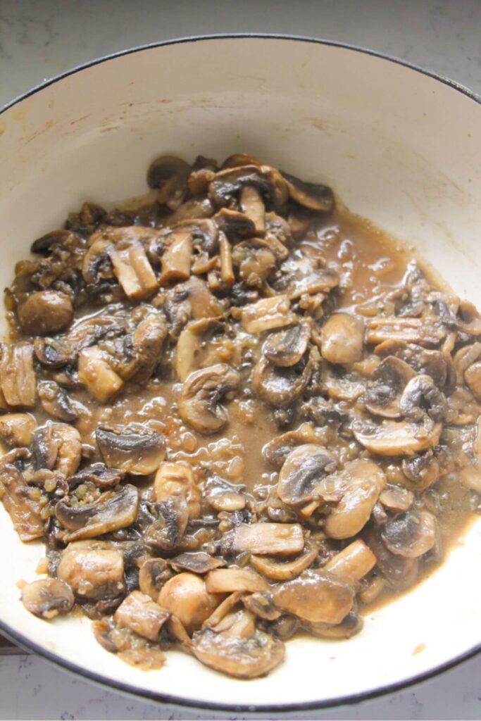 Sliced mushrooms with white wine in a large white skillet.
