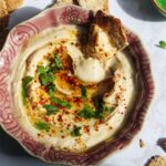 Cracker swirled through white bean dip in a small pink bowl with more crackers on the side.