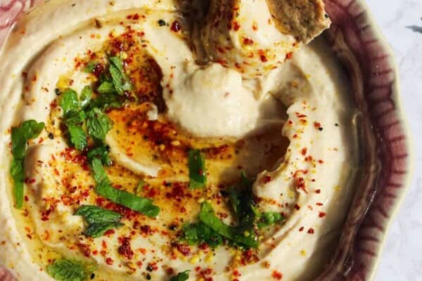 Cracker swirled through white bean dip in a small pink bowl with more crackers on the side.