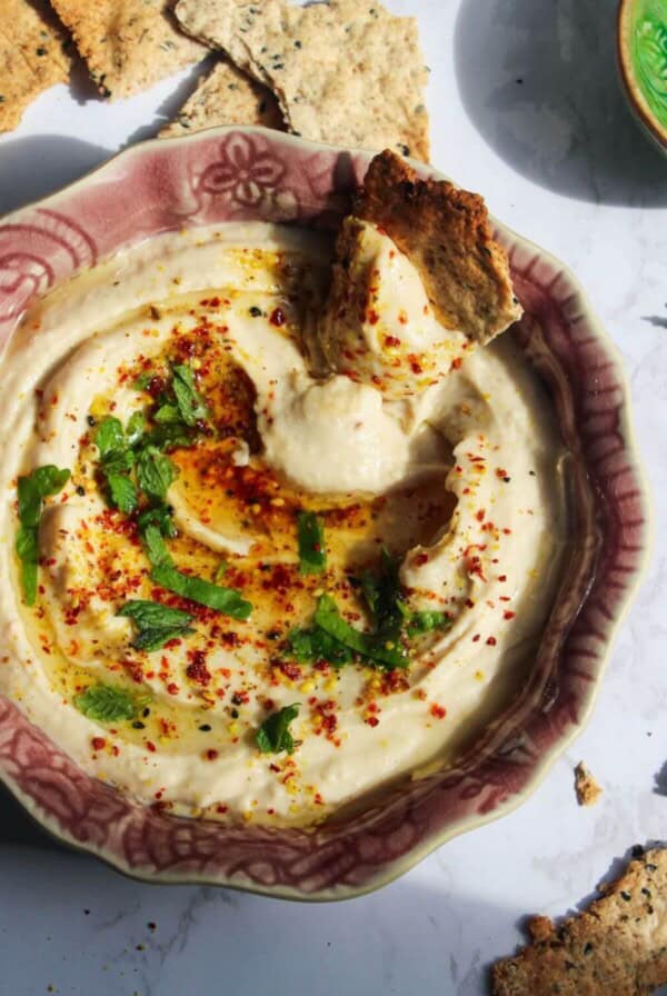 Cracker swirled through white bean dip in a small pink bowl with more crackers on the side.