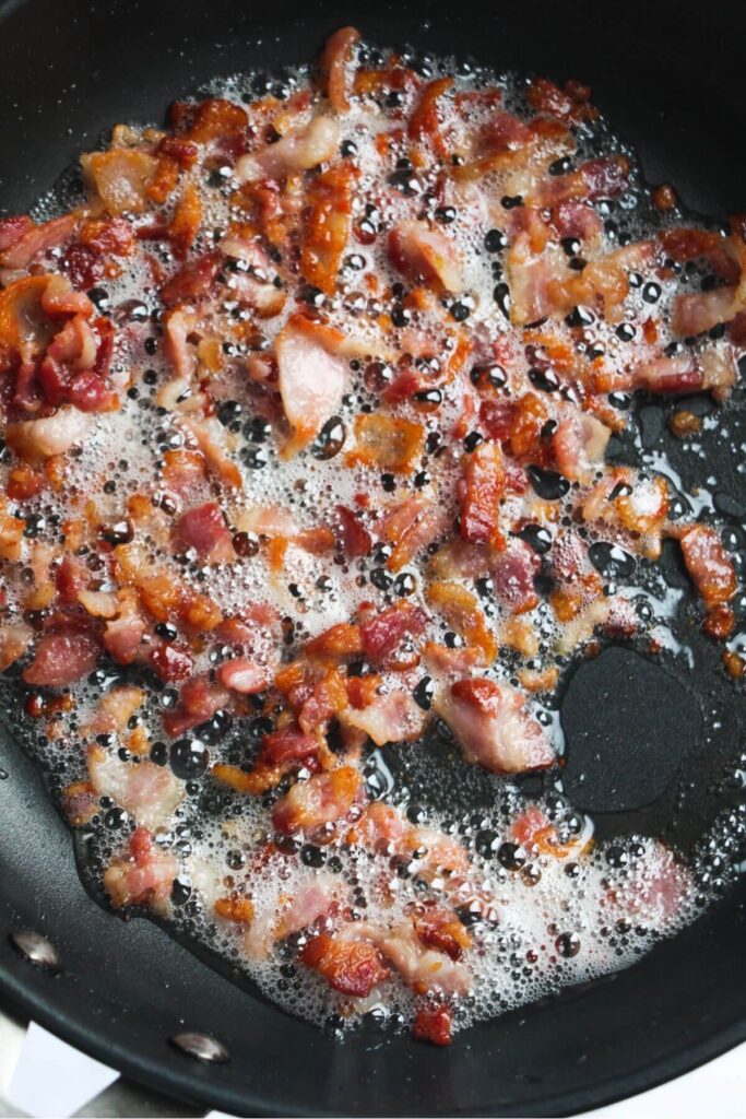 Chopped bacon cooking in a small black pan.