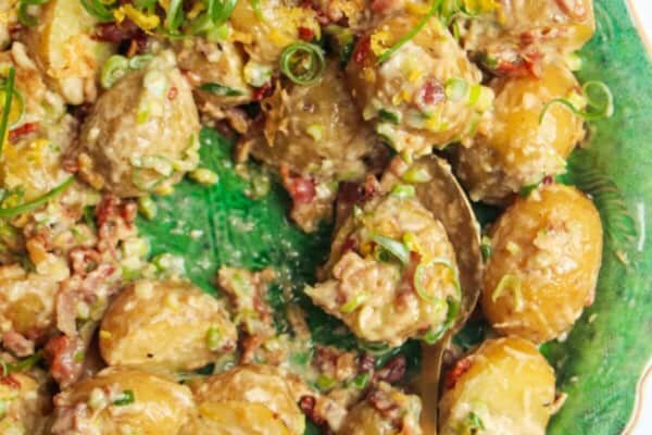 Close up of creamy Caesar potato salad on a large green serving plate with more Caesar dressing on the side.