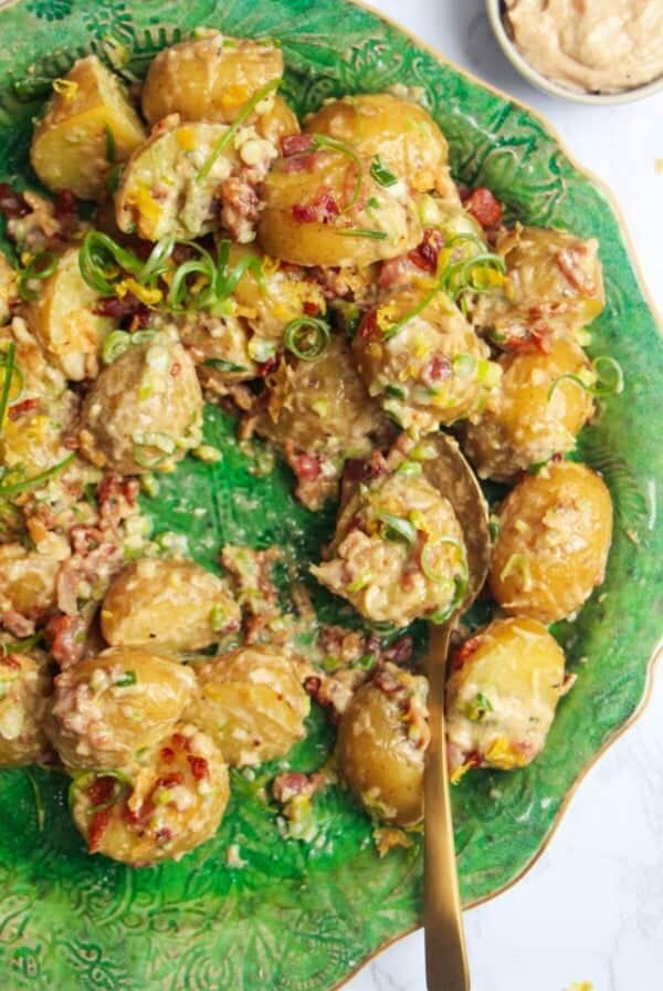 Close up of creamy Caesar potato salad on a large green serving plate with more Caesar dressing on the side.