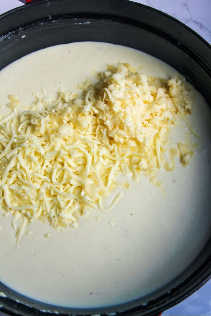 Grated cheese added to bechamel in a large pan.