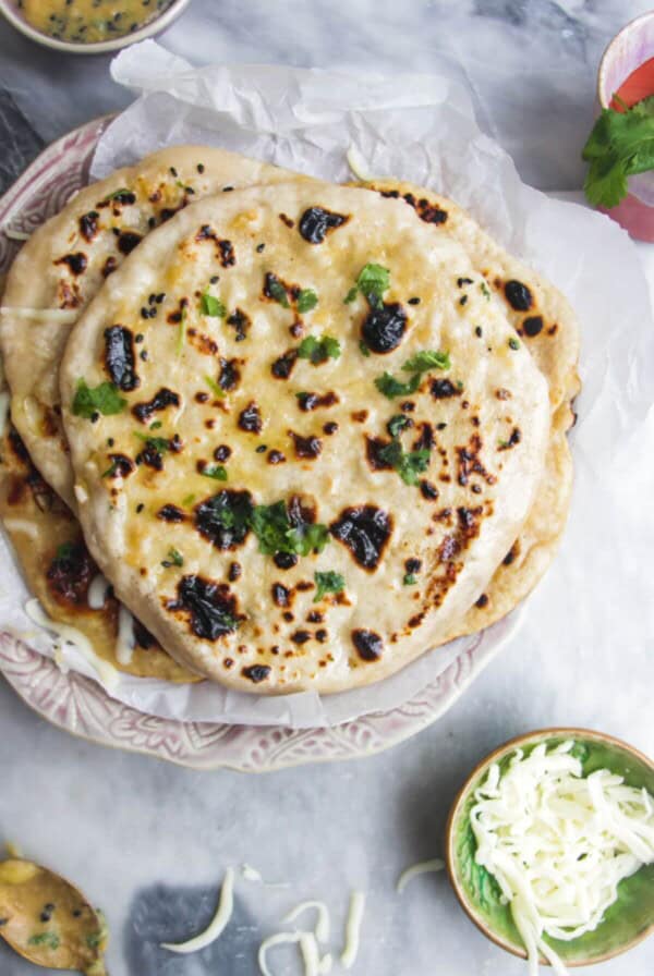 A pile of cheese naan on a small pink plate with a small bowl of grated cheese and butter on the side.