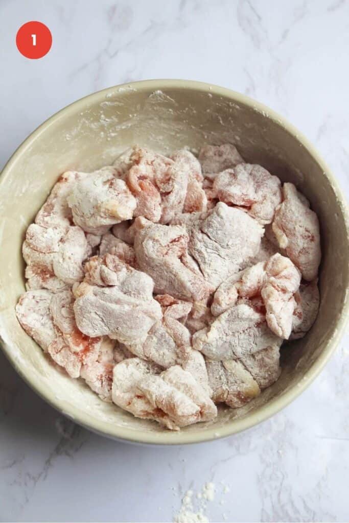 Chicken pieces tossed in cornstarch in a bowl.