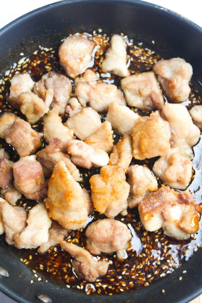 Pan-fried chicken pieces added to a frying pan with honey sesame sauce.
