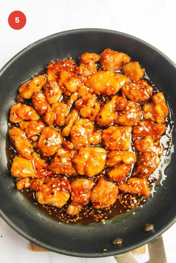 Chicken tossed through honey sesame sauce in pan.