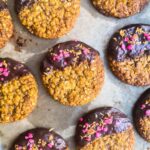 Chocolate dipped Anzac biscuits topped with rose and coconut on a lined tray.