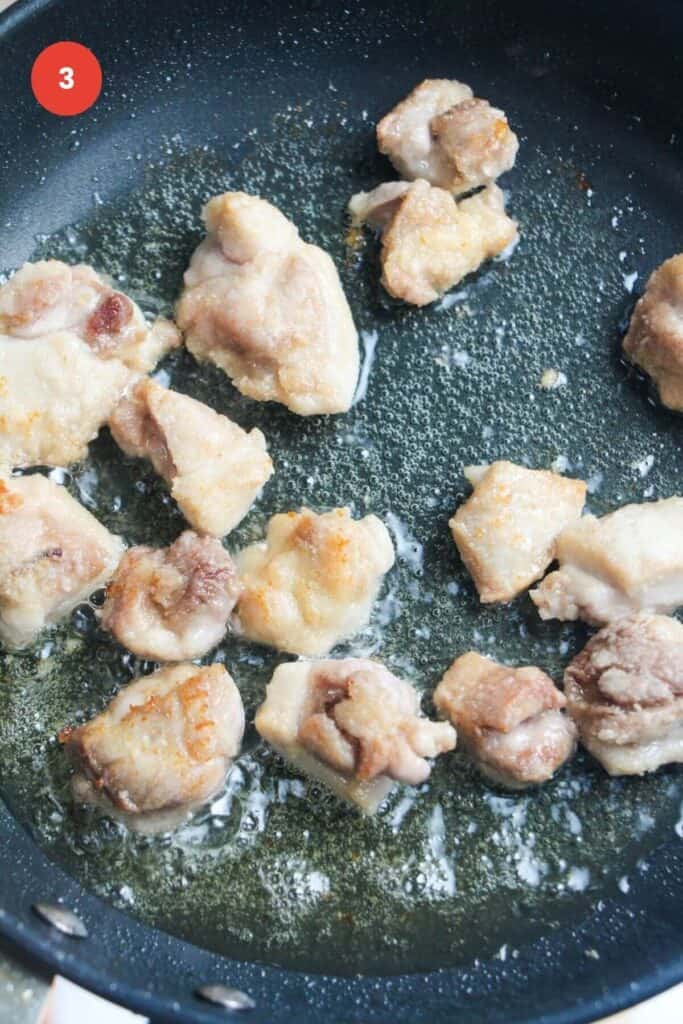 Chicken pieces cooking in pan.