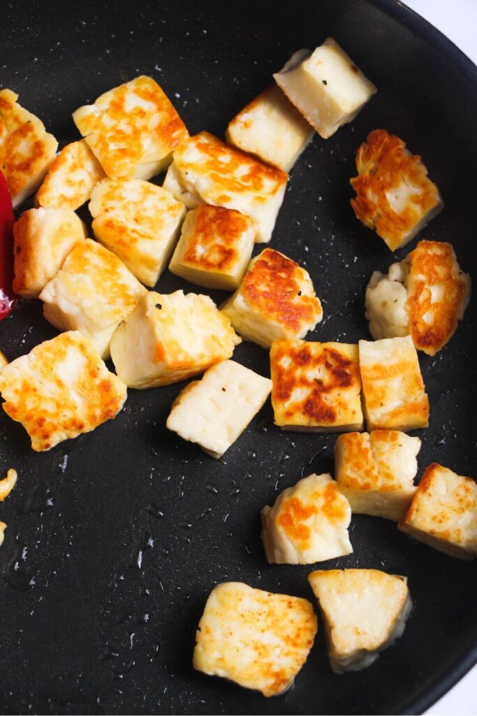 Golden cubes of halloumi in a black frying pan.