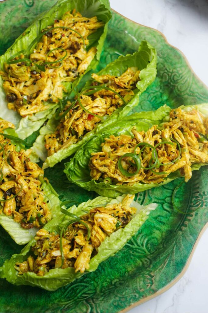 Five lettuce leaves stuffed with coronation chicken on a large green platter.