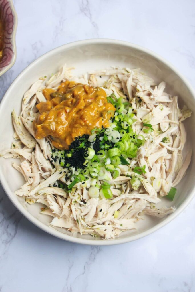 Shredded chicken, scallions, nigella seeds and coronation sauce in a small white bowl.