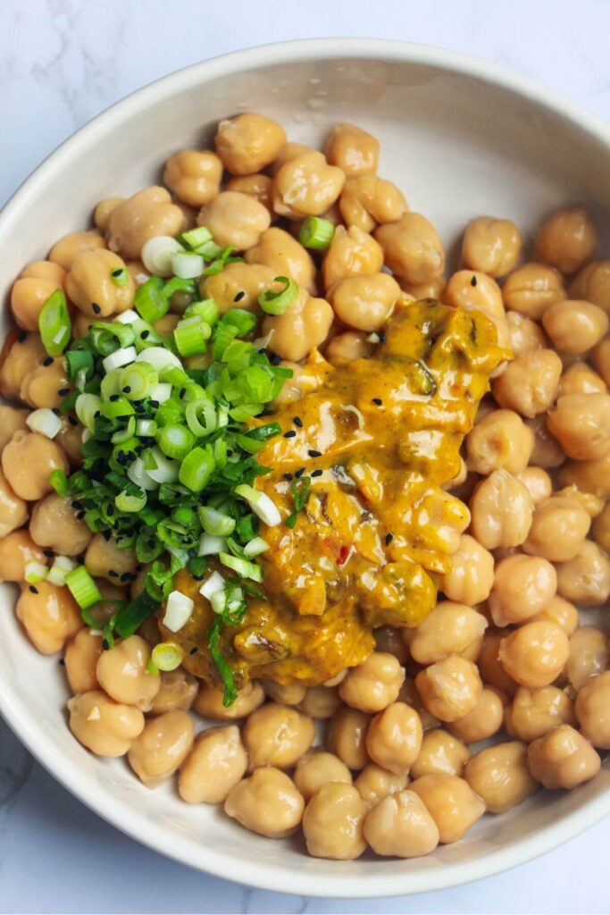 Chickpeas, scallions, nigella seeds and coronation sauce in a small white bowl.