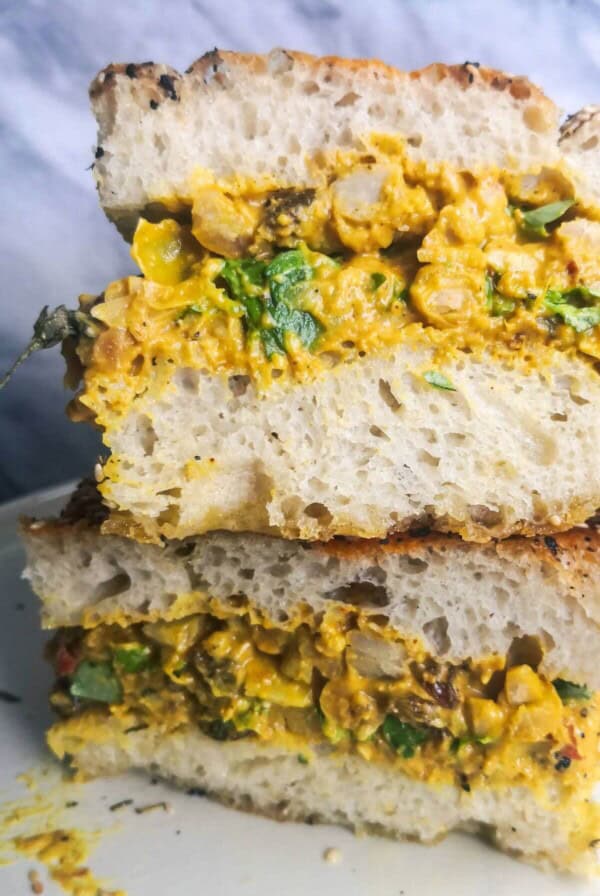 Two coronation chickpea stuffed focaccia sandwiches on top of each other on a white plate.