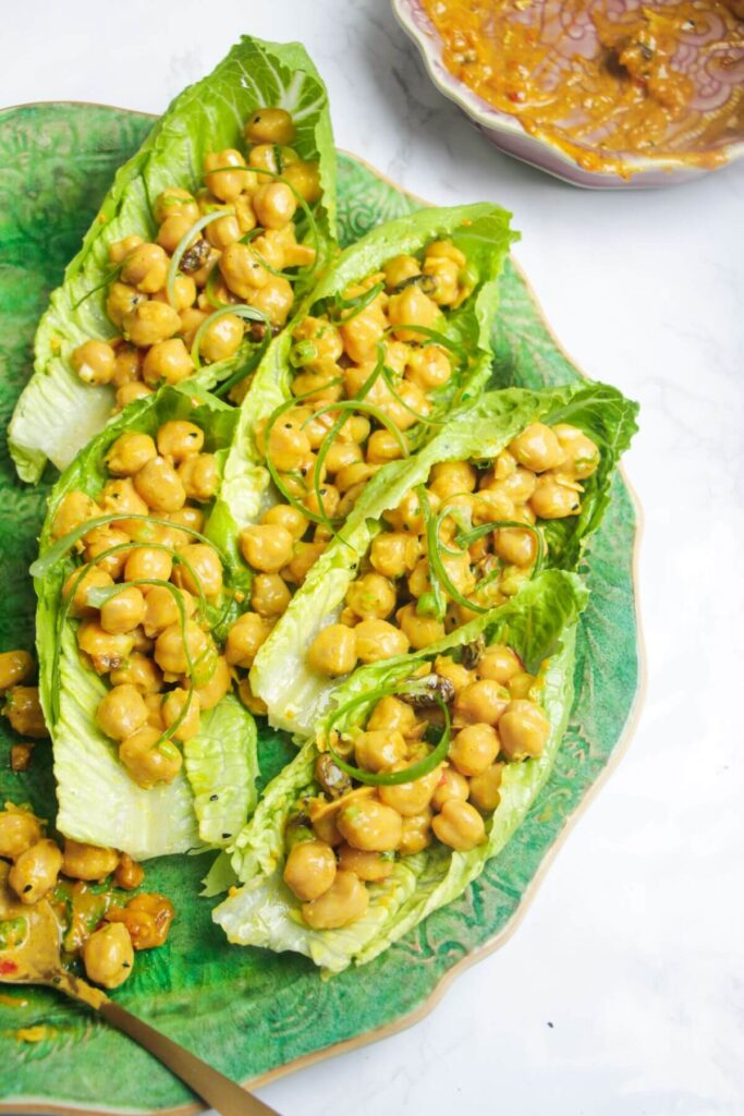 Curried coronation chickpeas in green lettuce leaves on a green platter.