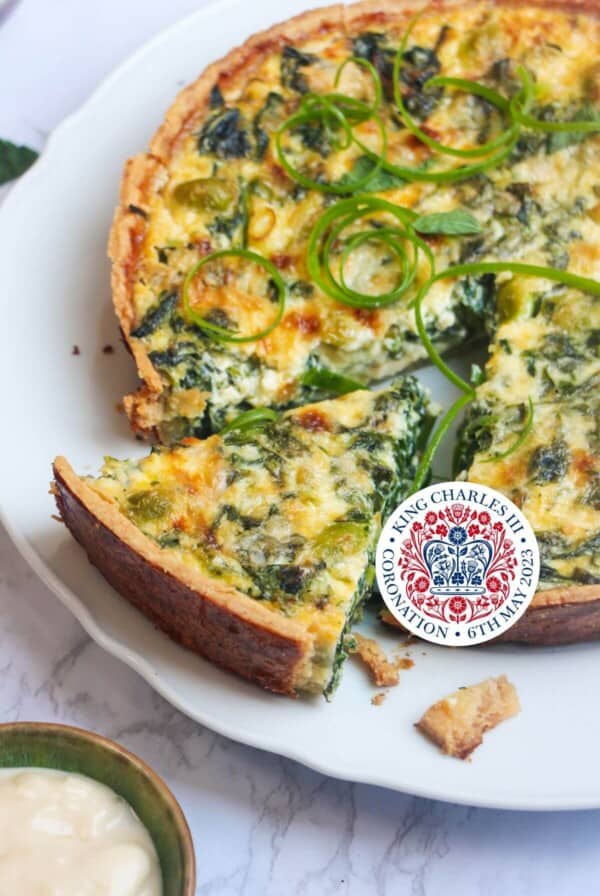 Coronation quiche on a scalloped white plate with a piece cut out of it.