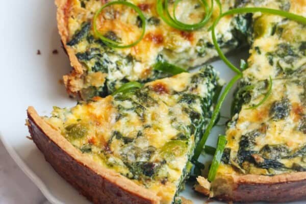 Coronation quiche on a scalloped white plate with a piece cut out of it.