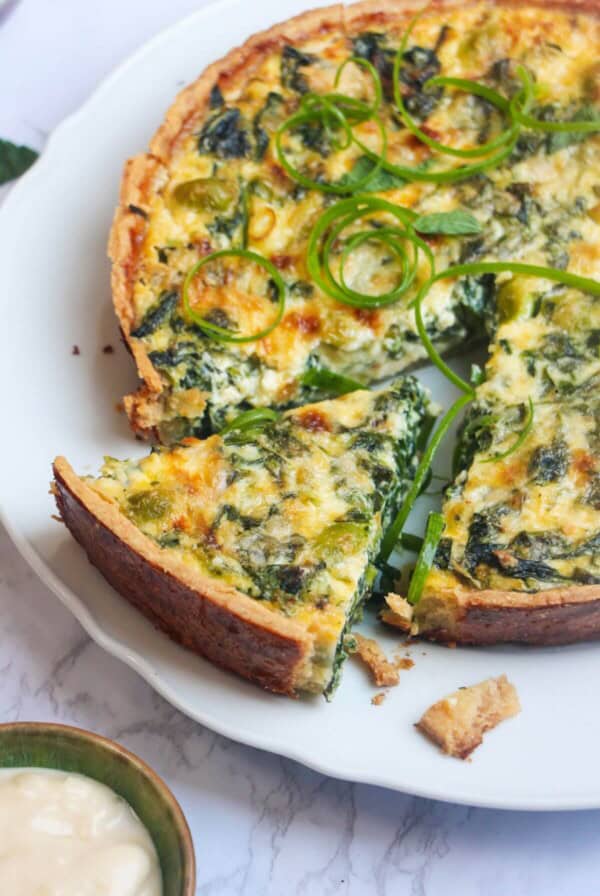 Coronation quiche on a scalloped white plate with a piece cut out of it.