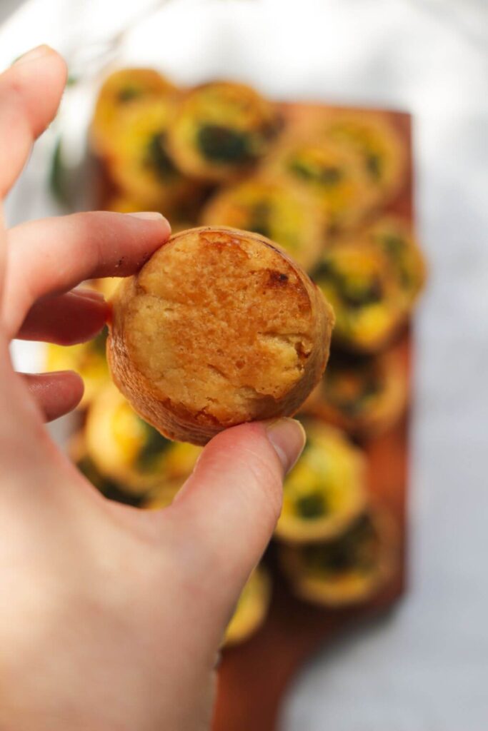 Hand holding up a mini coronation quiche, showing the crispy brown pastry shell.
