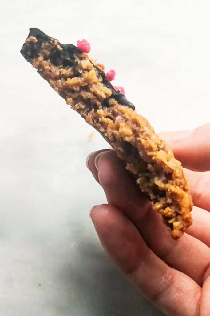 Close up of hand holding a broken in half Anzac biscuit.