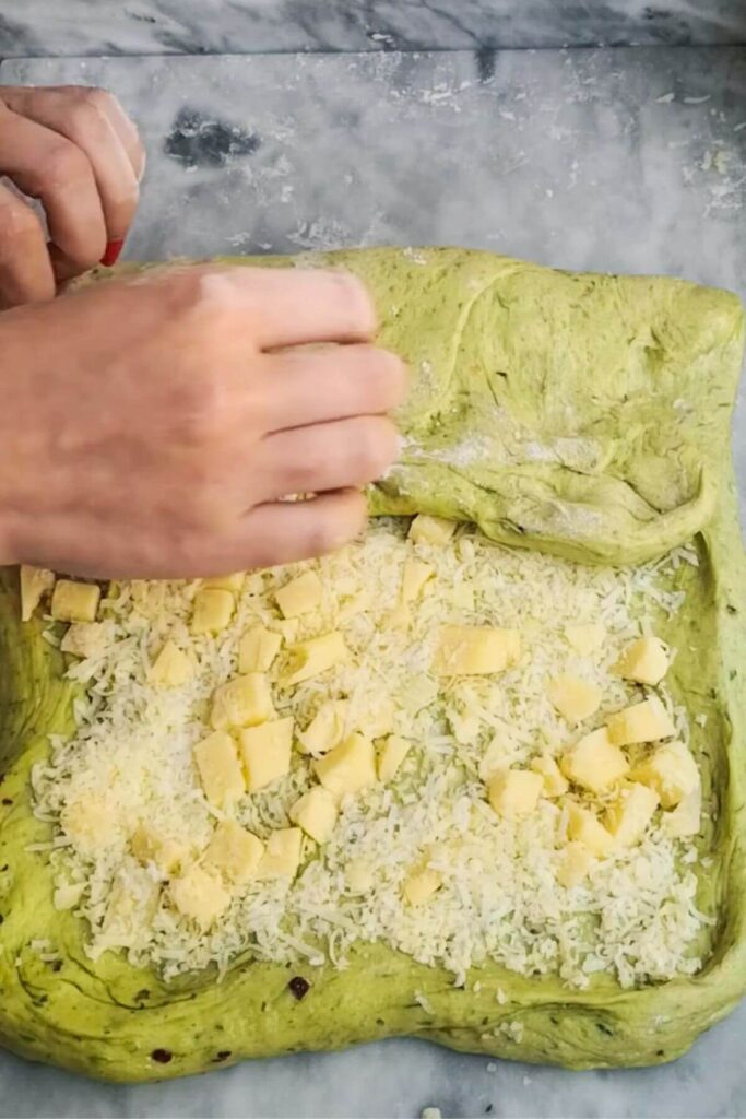 Hands folding cheese into dough on a grey marble background.