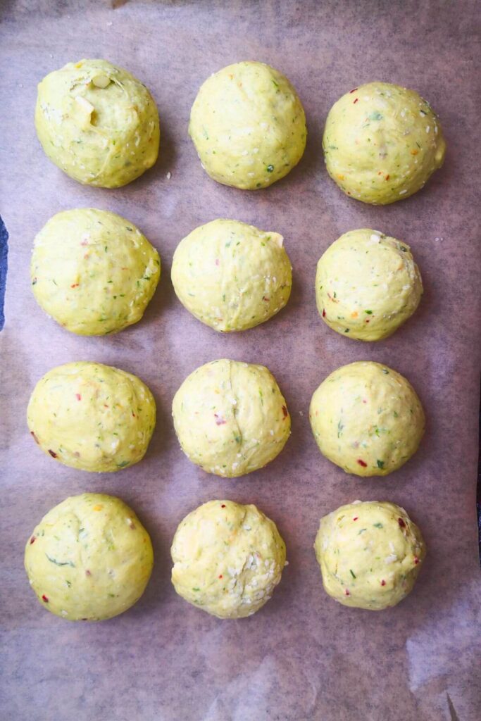 12 wild garlic hot cross bun dough balls on a lined baking tray.