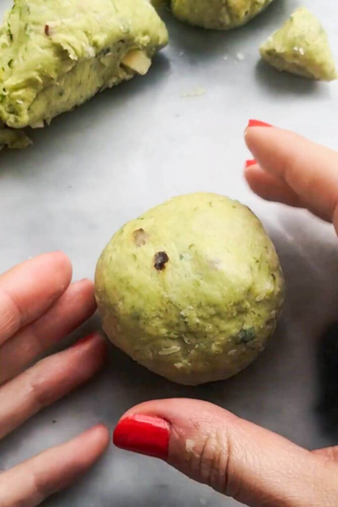 Hands forming a ball from wild garlic hot cross bun dough.