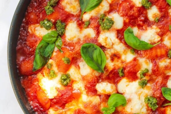 Mozzarella topped gnocchi alla sorrentina in a small frying pan, topped with basil leaves.