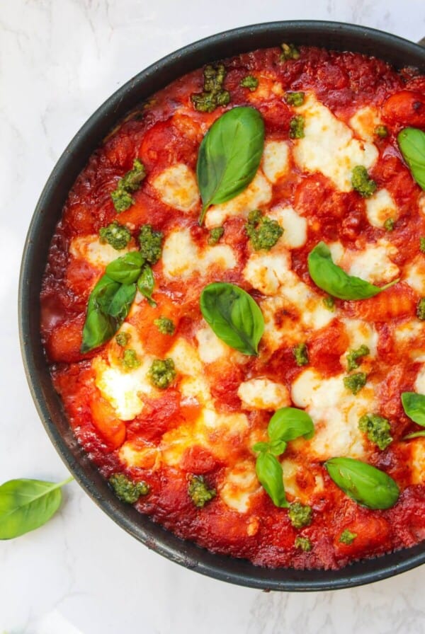Mozzarella topped gnocchi alla sorrentina in a small frying pan, topped with basil leaves.