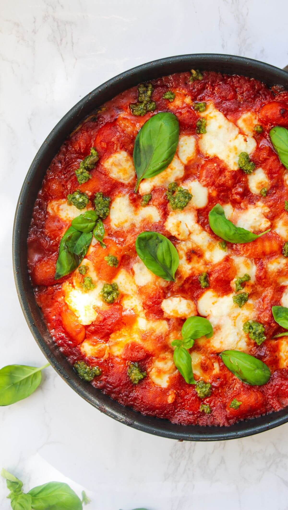 Mozzarella topped gnocchi alla sorrentina in a small frying pan, topped with basil leaves.