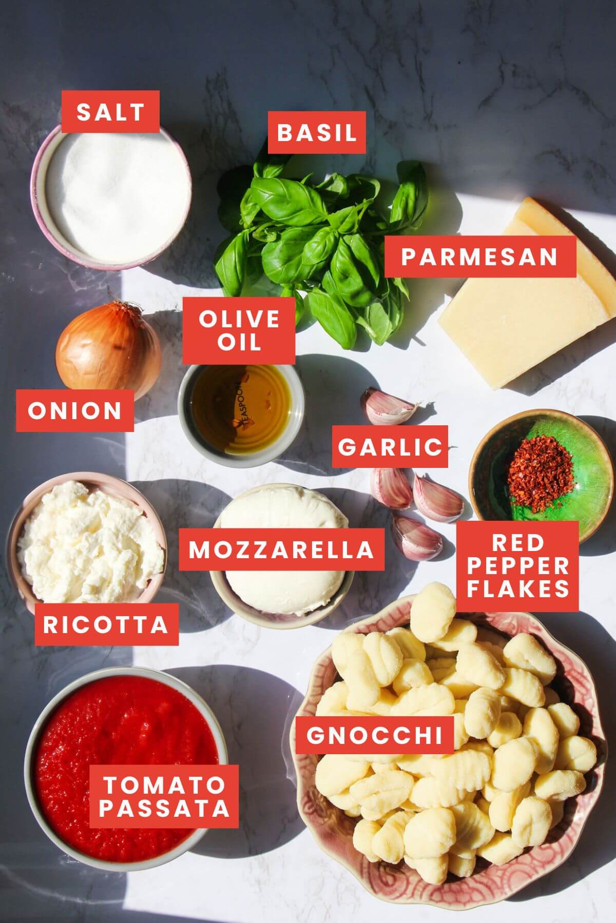 Ingredients for gnocchi alla sorrentina laid out on a white marble background and labelled.