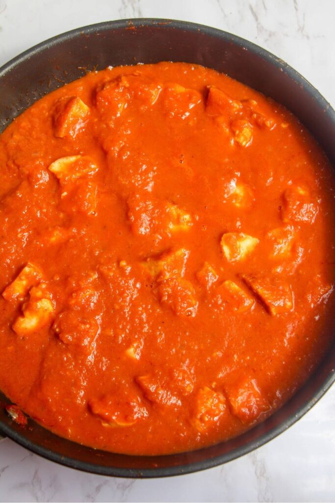 Halloumi mixed into tomato curry sauce in a black pan.